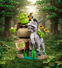 A building block set depicting Shrek and Donkey on a stylized base with flowers, green plants, and a sign reading 'Beware Ogre'.