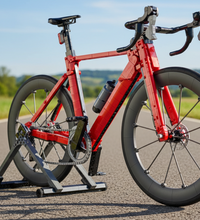 A red drop-bar road bicycle with black wheels and components, shown on a gray trainer against a plain white background.