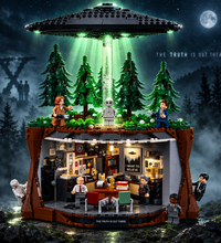 A detailed LEGO model set featuring a large black flying saucer hovering over a forest, with a brown cave-like structure below containing a detailed office scene. Multiple minifigures and small accessories are arranged around the set against a plain white background.