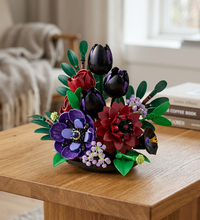 A LEGO-style floral bouquet set with black tulips, red roses, purple anemones, green leaves, and small lavender blossoms on a black base against a white background.