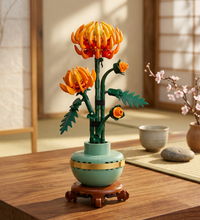 A LEGO floral sculpture of three stylized flowers with orange petals, green stems and leaves, set in a light green pot with a gold band, on a brown wooden base against a white background.