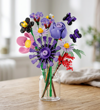 A colorful toy flower bouquet made from building blocks, featuring purple, pink, black, red, and lavender flowers with green stems on a plain white background.