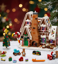 A gingerbread house building set with multiple Christmas-themed accessories, including a small tree, candy cane, trains, gift boxes, and minifigures, displayed on a clean white background.