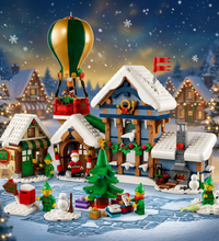 A LEGO Christmas village set featuring a snow-covered blue and brown cabin, a green and gold hot air balloon, a small tree, sledding, and festive figures on a white background.