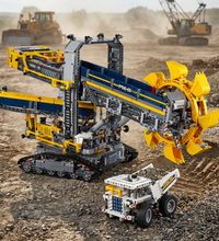 A Technic construction vehicle set featuring a large yellow and blue excavator with a rotating bucket, shown alongside a white dump truck and small loose bricks on a plain white background.