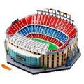 A detailed toy model of a stadium built from interlocking blocks, featuring red and blue tiered seating, a green field, beige stands, and a gray base. An orange accessory piece is placed in the lower-left corner on a plain white background.